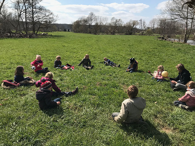 Photo d'un groupe d'enfants assis en cercle au milieu d'une prairie pour prendre une pause déjeuner